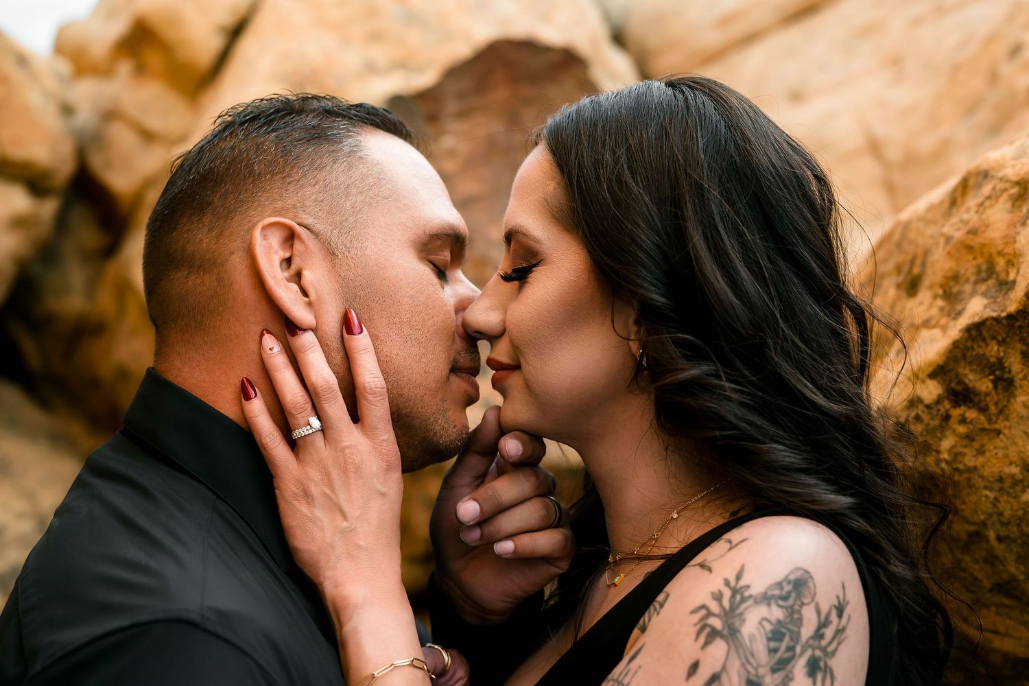 Couple sharing an intimate kiss while holding hands near rustic rock formations outdoors.