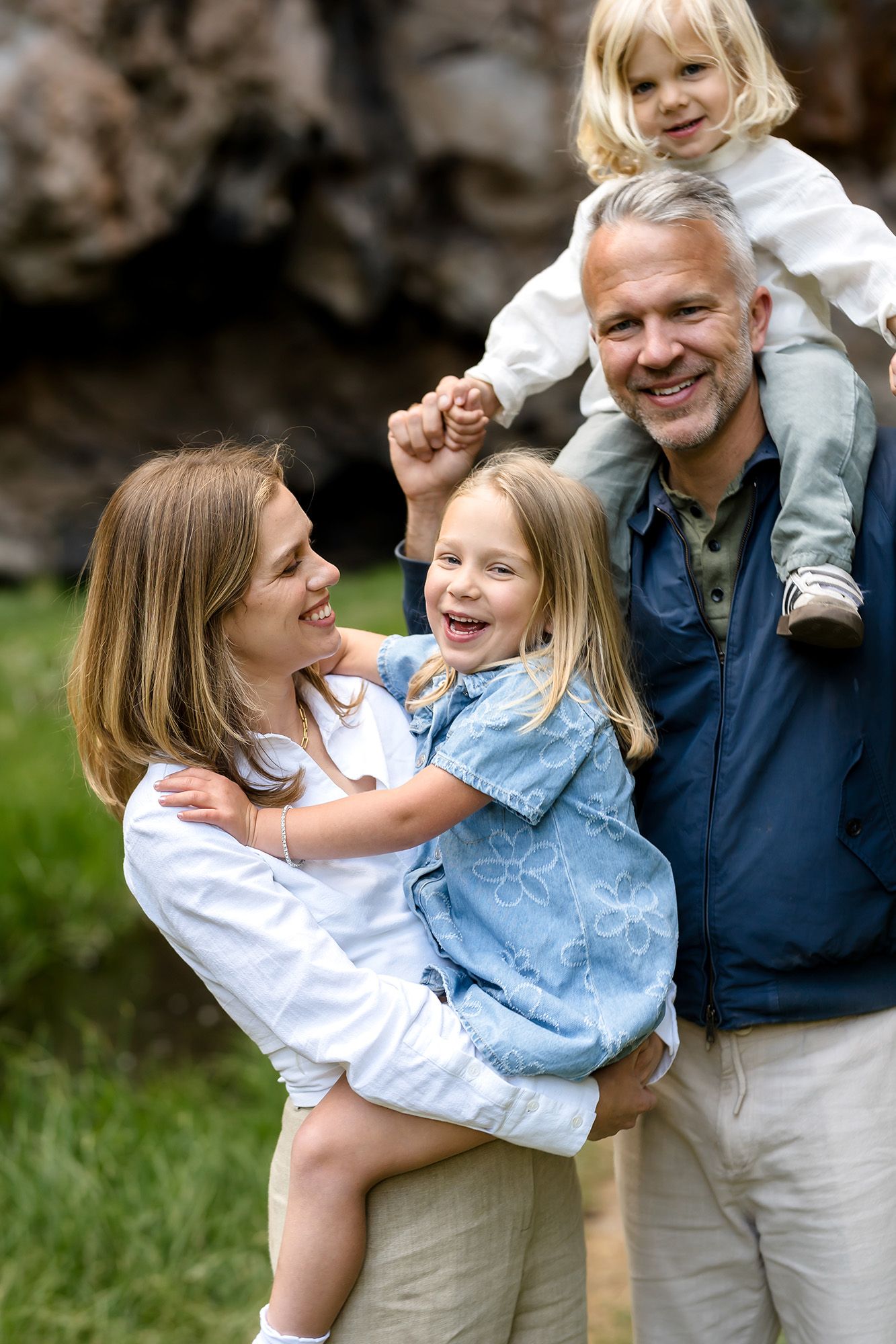 Happy family of four enjoying outdoor time, parents holding two young blonde girls while smiling and laughing together.