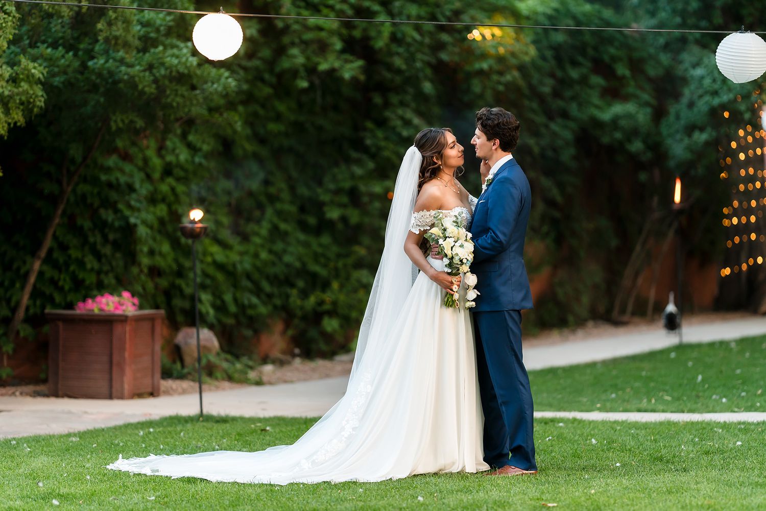 Bride and groom share a romantic moment outdoors at a garden wedding, surrounded by string lights and lush greenery.