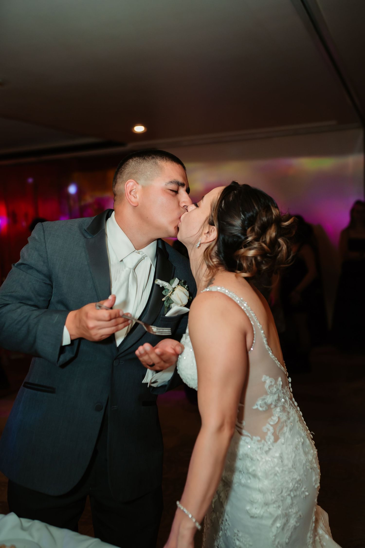 Couple sharing an intimate moment during their wedding reception with colorful party lights in background.