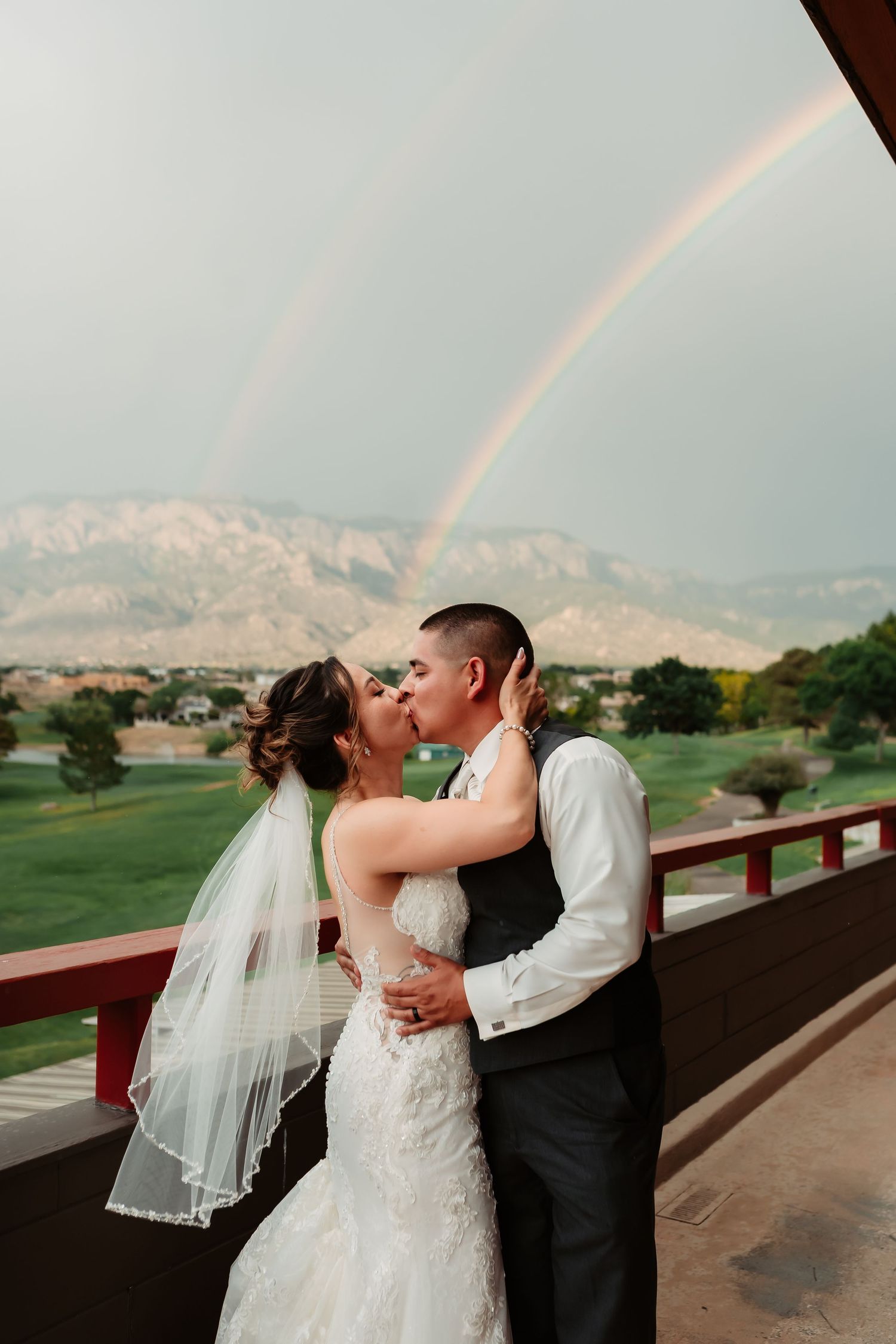 Wedding couple sharing a romantic kiss on a scenic overlook with mountains in the background.