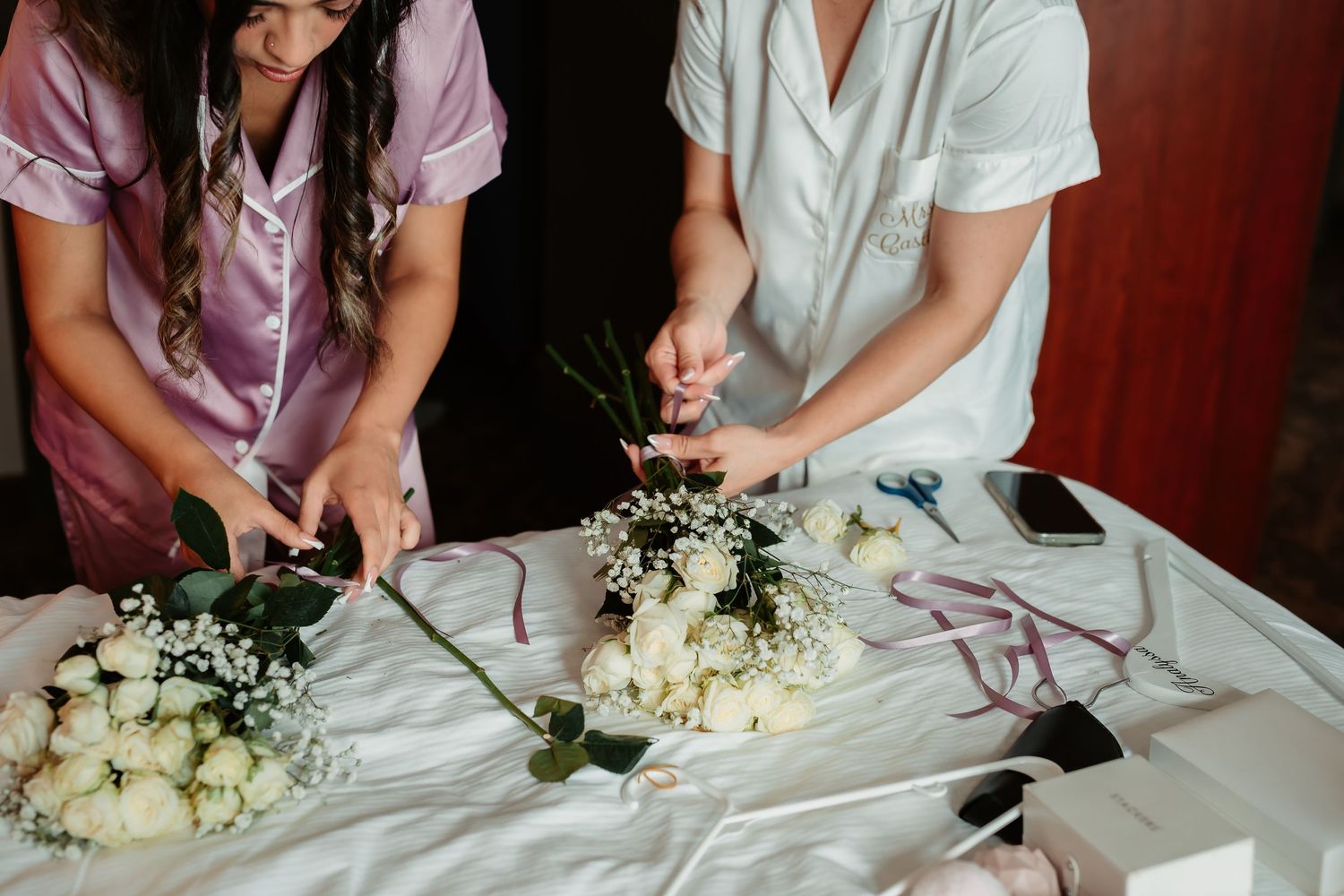 A person wearing a white shirt carefully selects and arranges white flowers and buds on a table during a floral workshop.