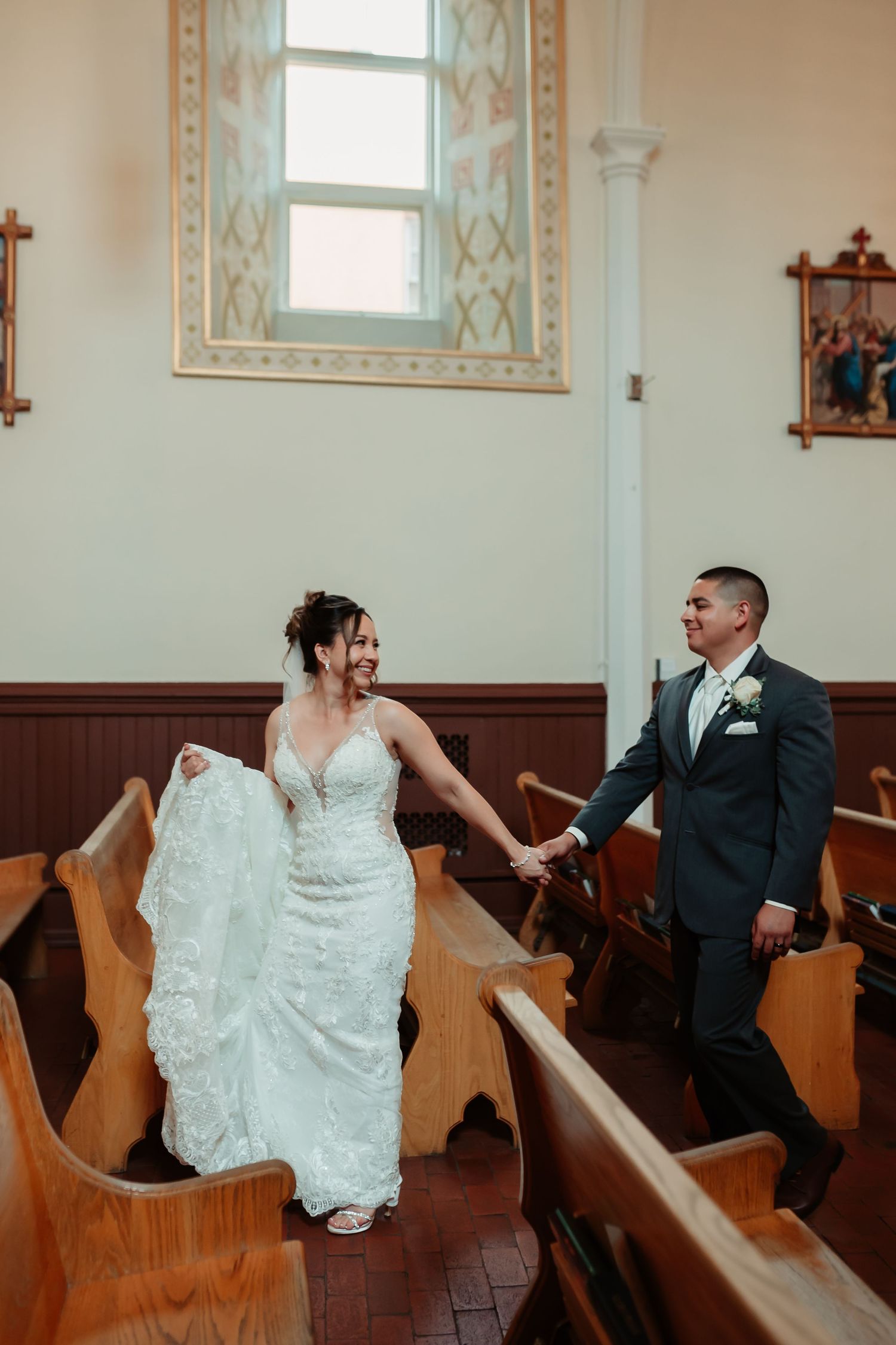 A couple in wedding attire shares playful moments while sitting in vintage wooden church pews.