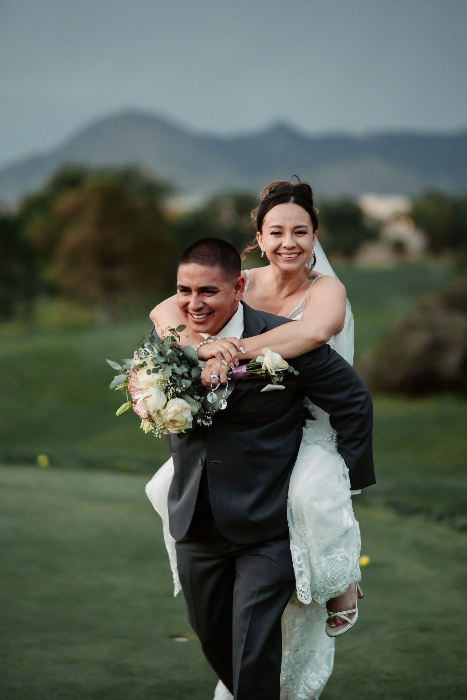 Joyful wedding couple sharing playful moment on grassy hillside at dusk.