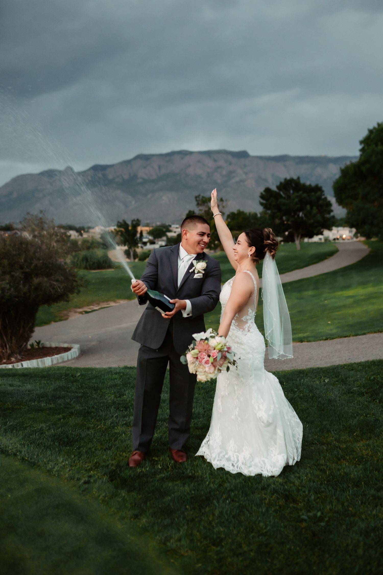 Wedding couple celebrating with champagne spray on a hilltop with mountain views.