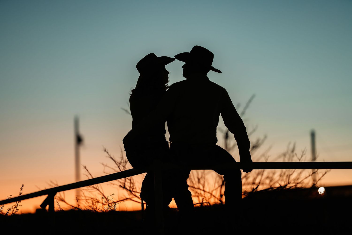 Dark silhouettes of ranchers on horseback along a fence line against a blue dusk sky.