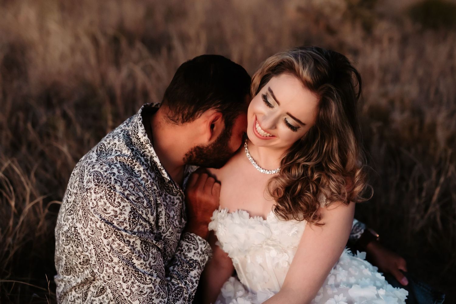 A romantic wedding couple embraces outdoors during golden hour in a natural setting.