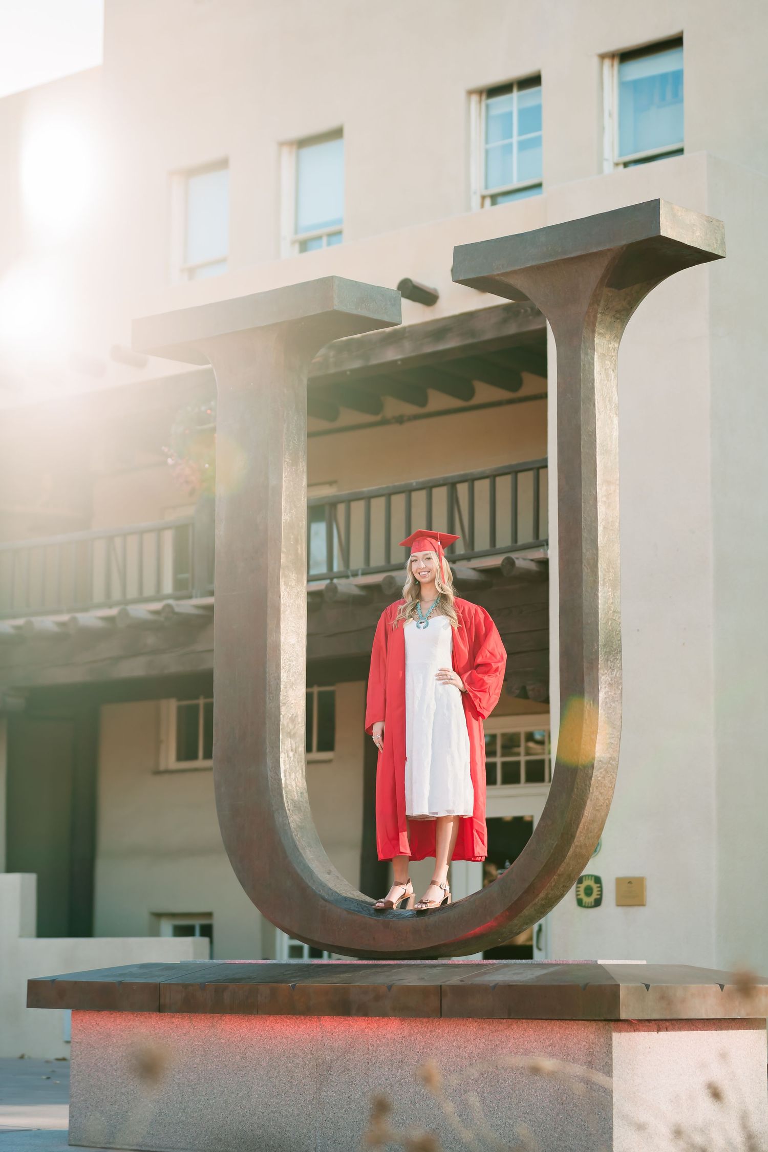 A person in a red jacket stands in front of a modern architectural structure with circular openings at sunset.