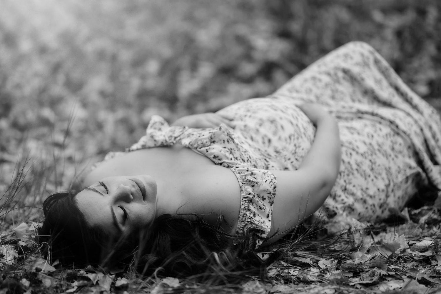 Black and white artistic portrait of someone lying among scattered leaves on the ground.