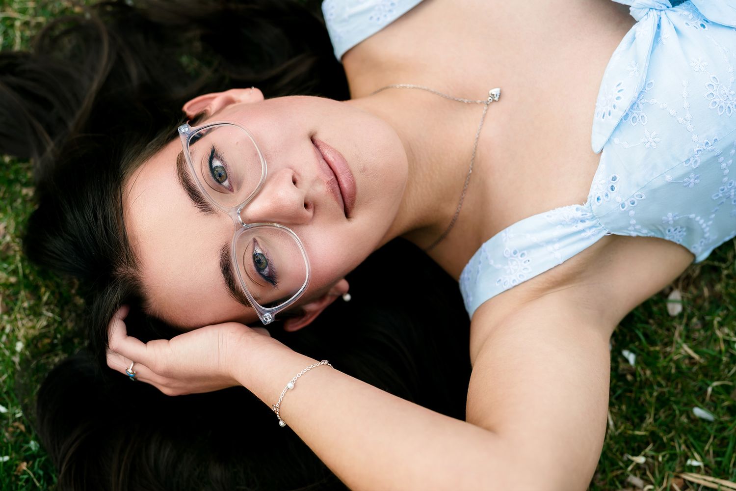 Person in white lace dress lying in grass and flowers during an outdoor portrait session.
