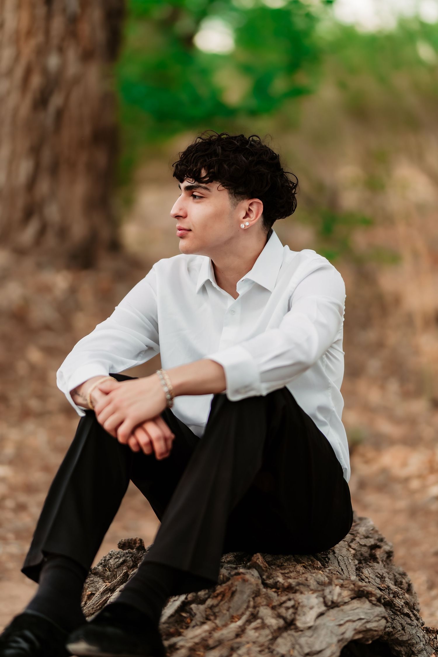 Person in white shirt sitting on tree trunk in nature setting with contemplative pose.