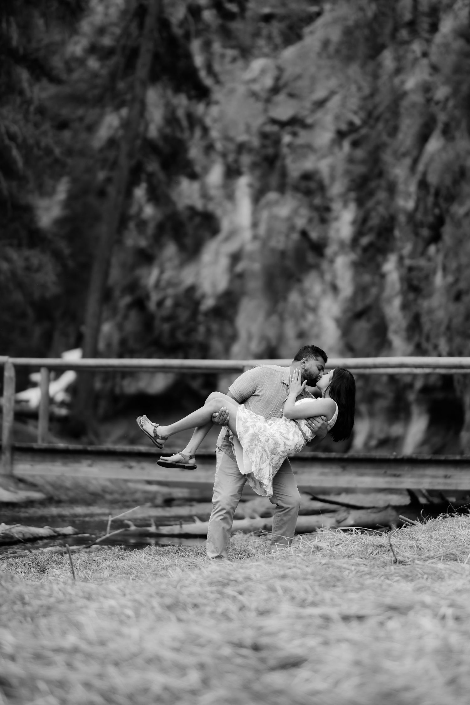 A romantic couple embraces in a dramatic dip pose outdoors against a mountainous backdrop in black and white.