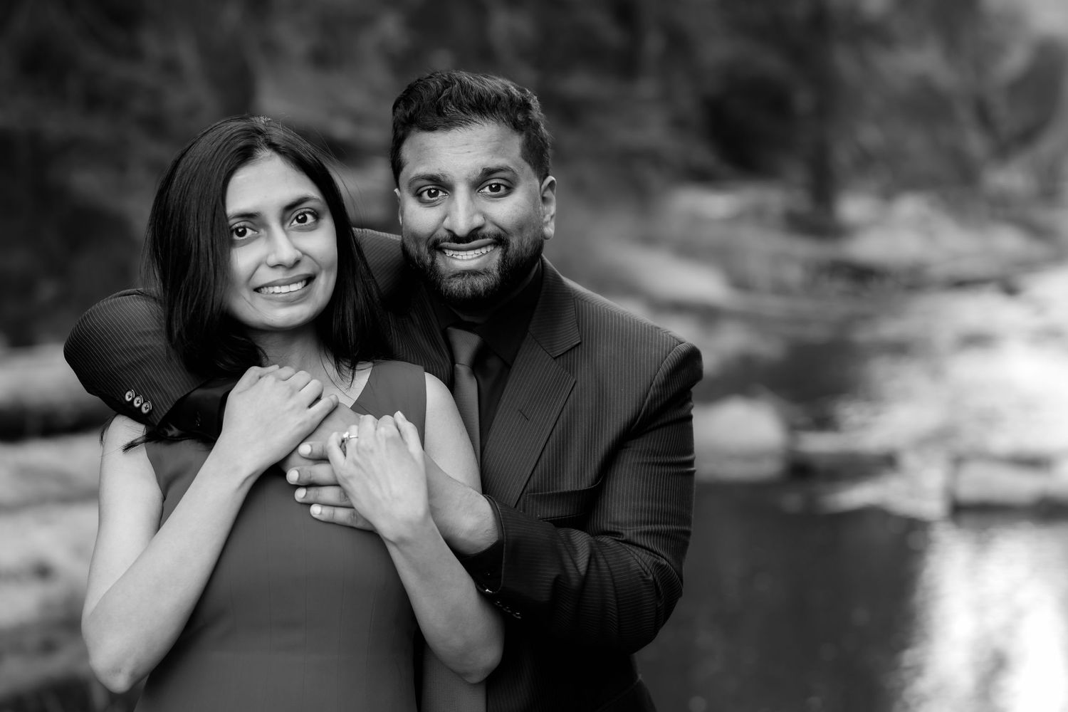 A black and white engagement portrait with a natural backdrop.