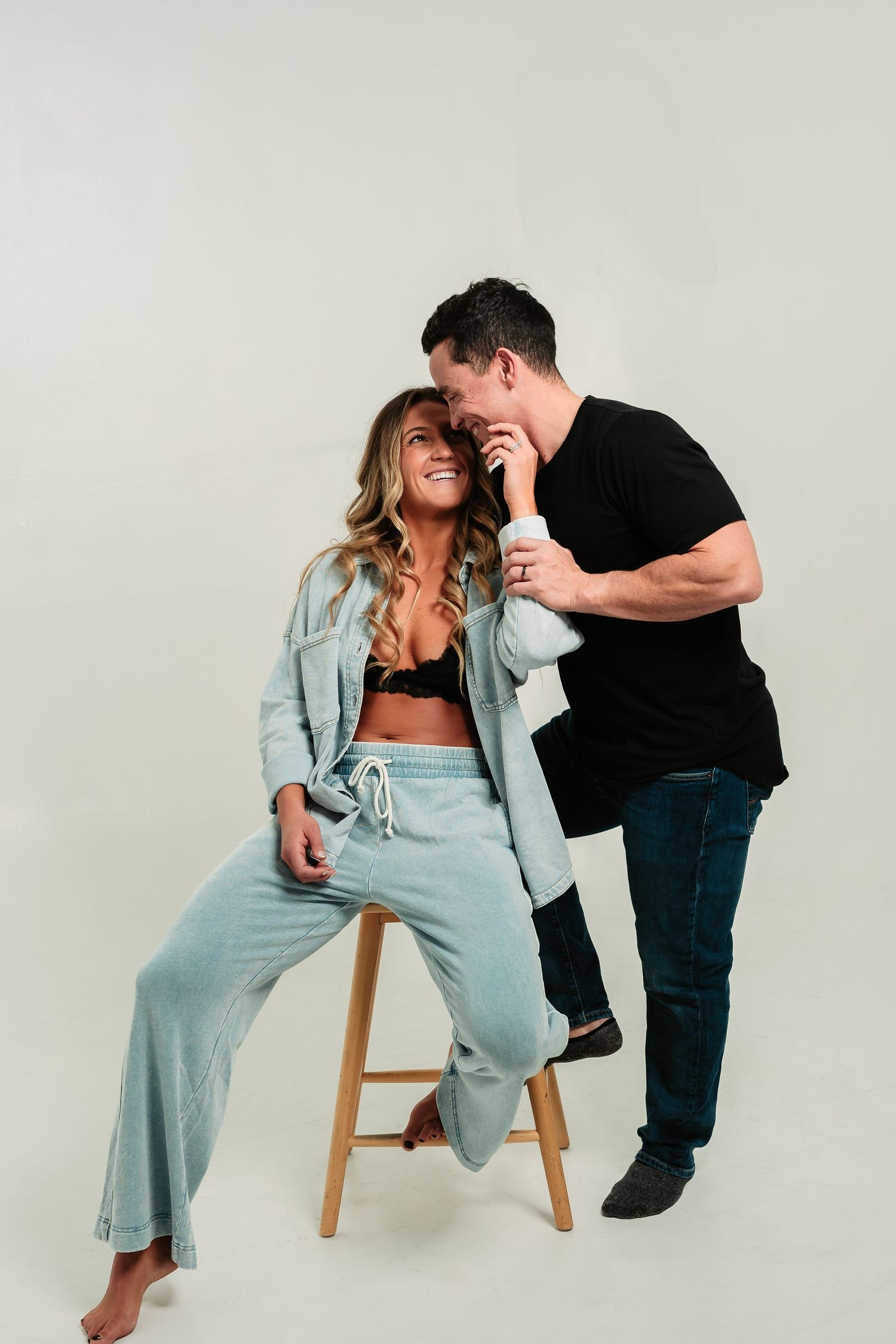 Intimate photoshoot featuring casual interaction between two people in a minimalist white studio setting.