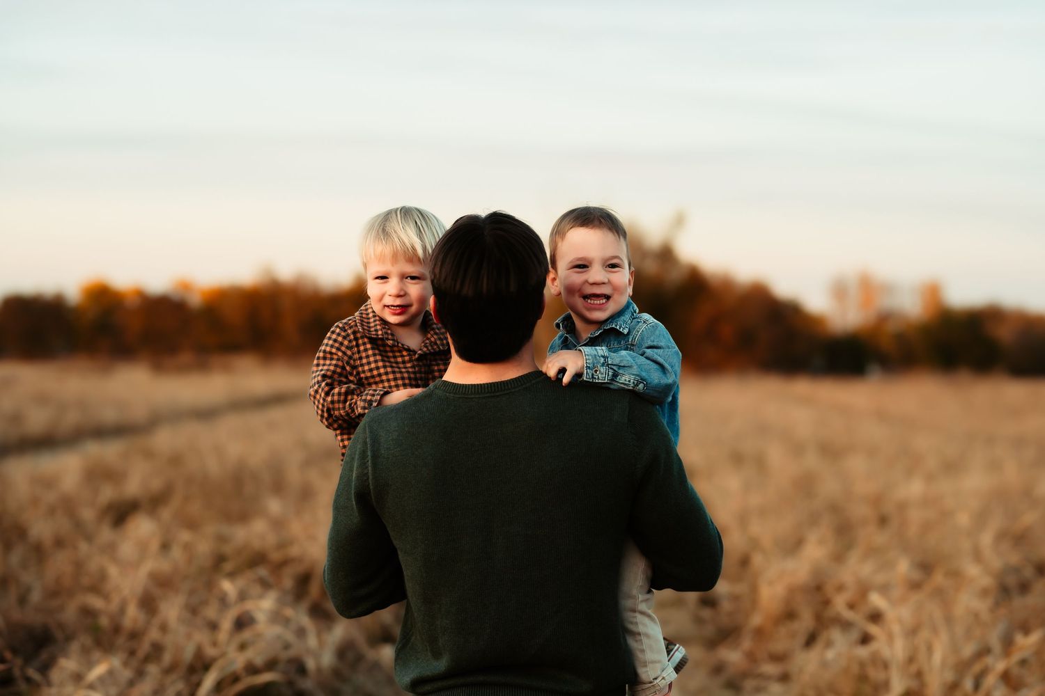 A family shares joyful moments together in a golden autumn field at sunset.