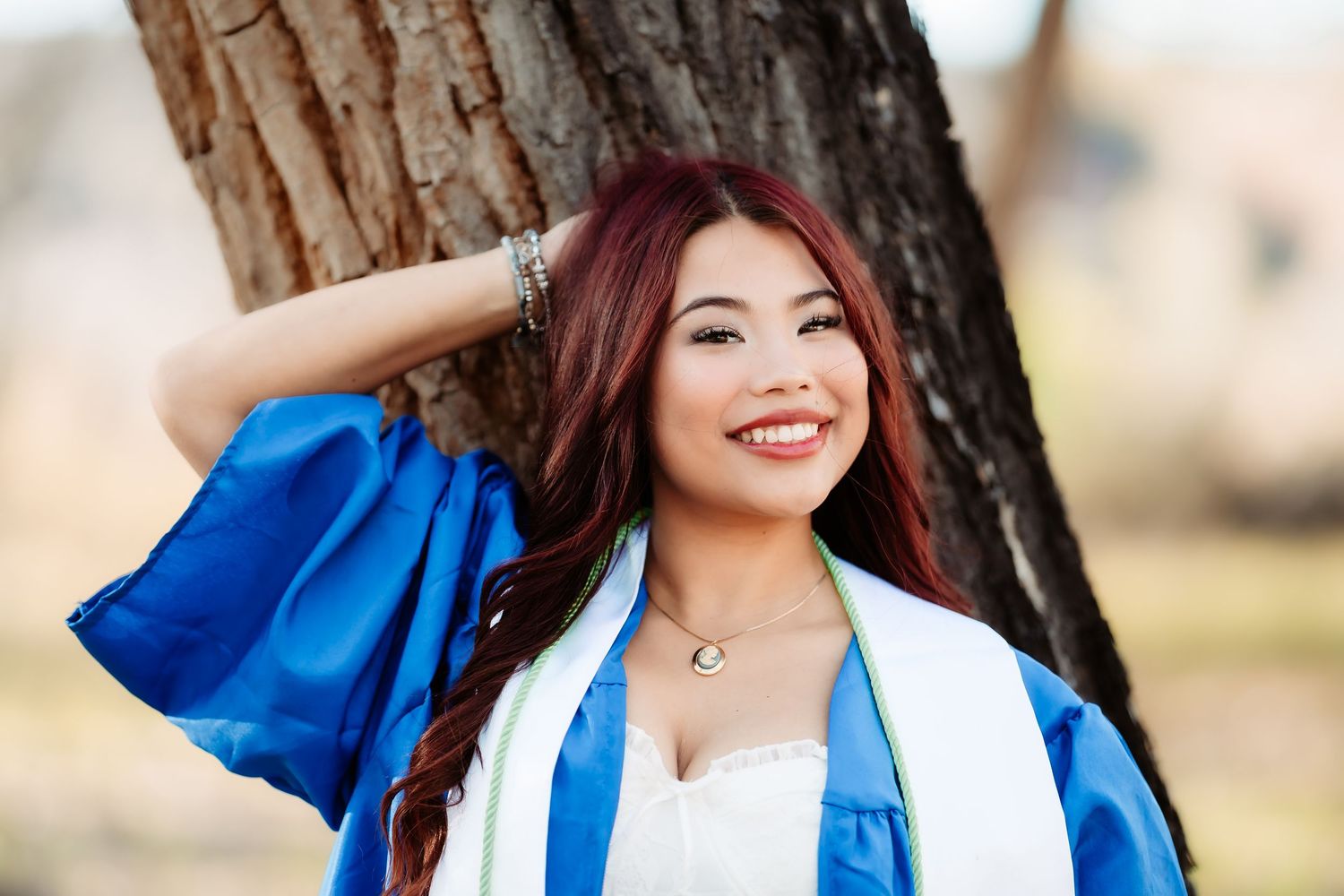 Woman in bright blue graduation gown smiles joyfully during outdoor photo session.