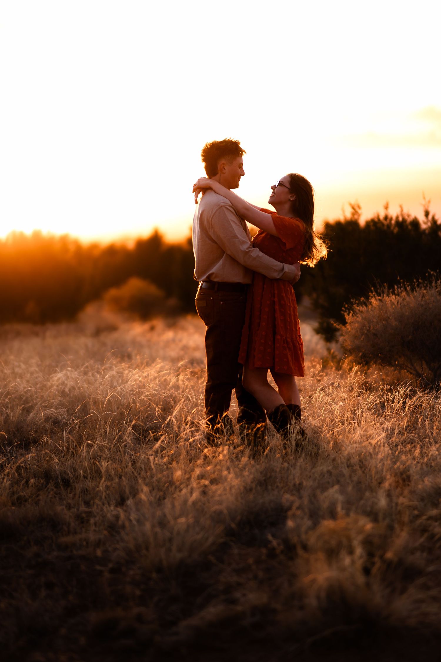 Silhouettes of a couple dancing in a golden field at sunset with tall grass illuminated by warm sunlight.