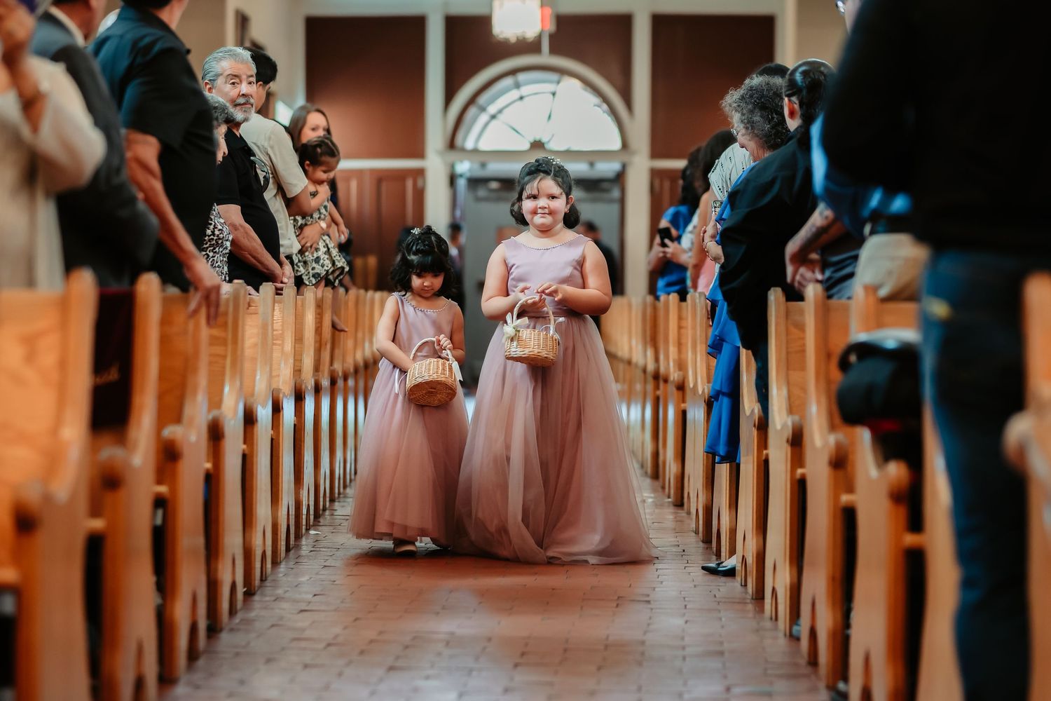Guests seated in wooden church pews for a wedding ceremony with soft lighting illuminating the aisle.