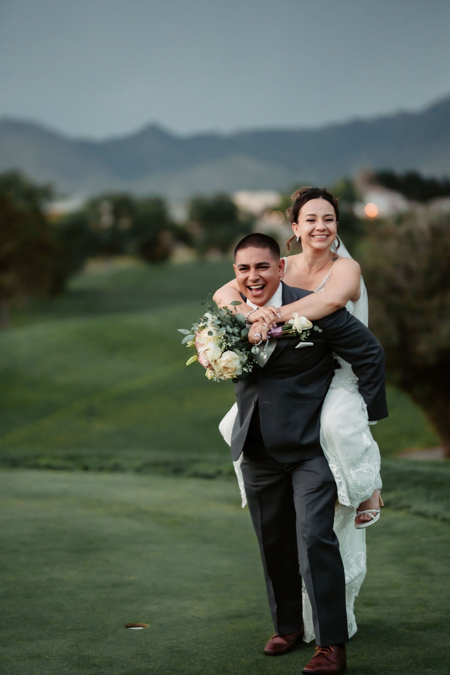 Playful wedding couple laughing together on lush green golf course.