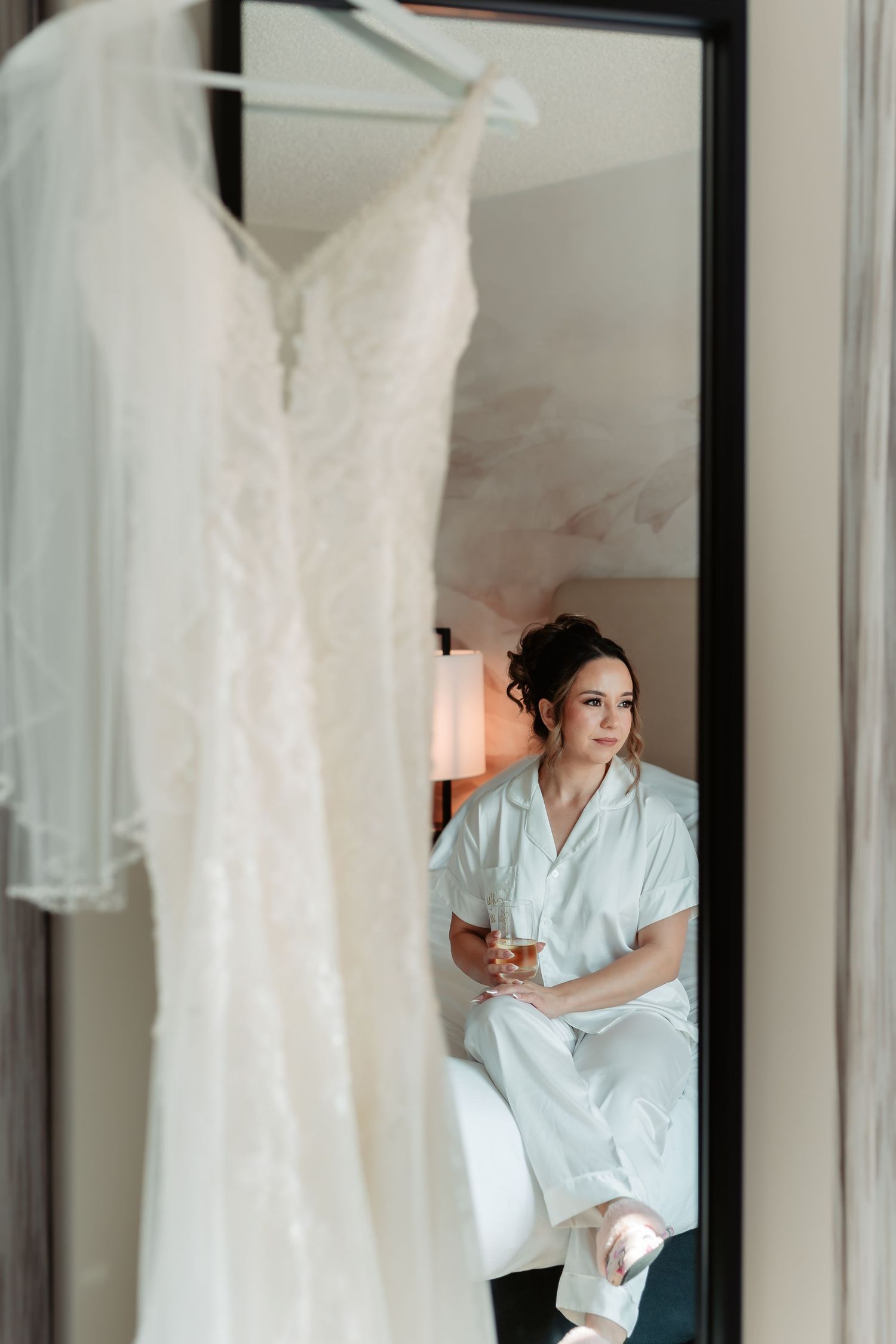 White wedding dress displayed on hanger with morning light streaming through curtained windows.