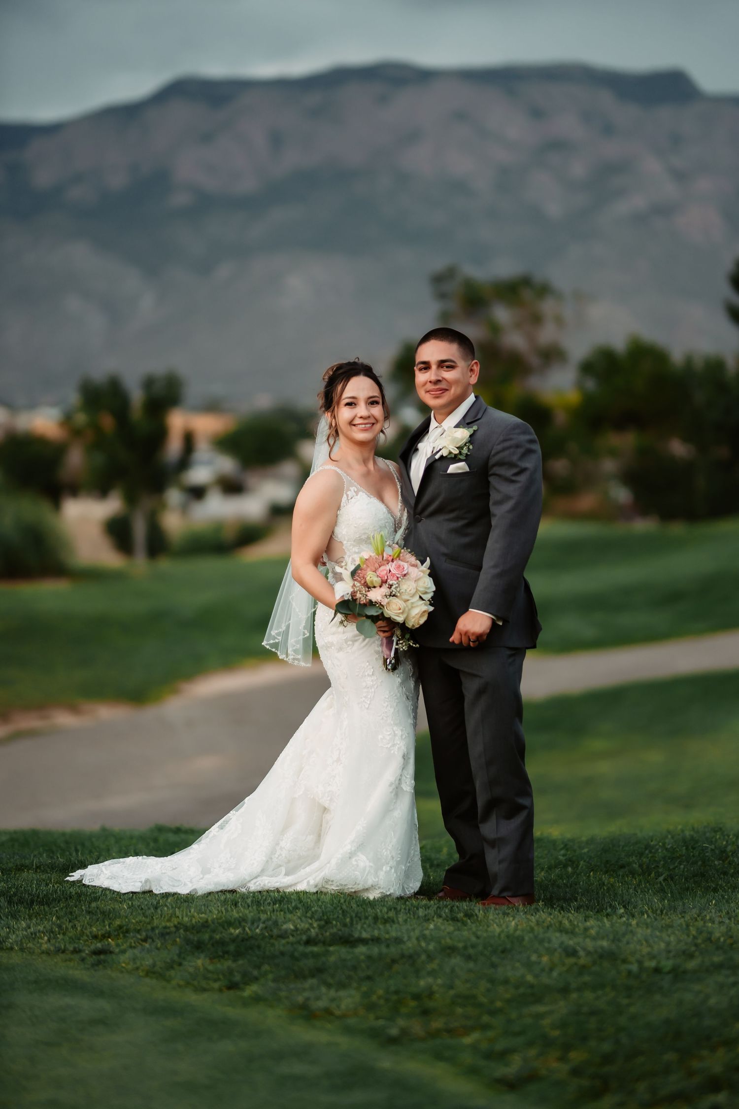 Newlyweds share candid moments while walking across a golf course with mountains in the background.