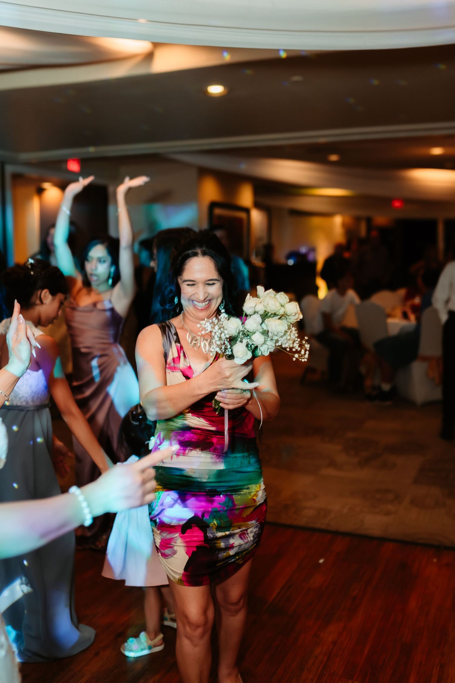 Dance floor filled with guests celebrating at wedding reception with blue mood lighting and hardwood floors.