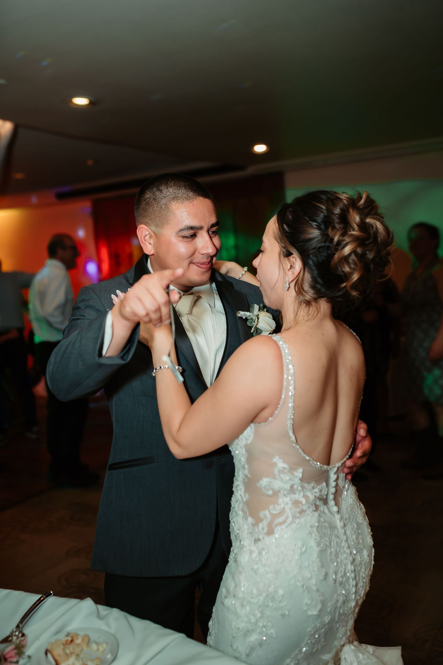 A couple shares an intimate dance in formal attire at their wedding reception under ambient lighting.