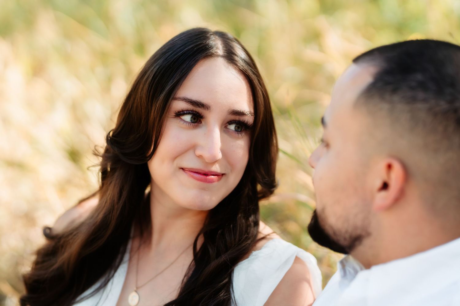 A couple shares a tender moment outdoors with golden grass in the background during an engagement photoshoot.