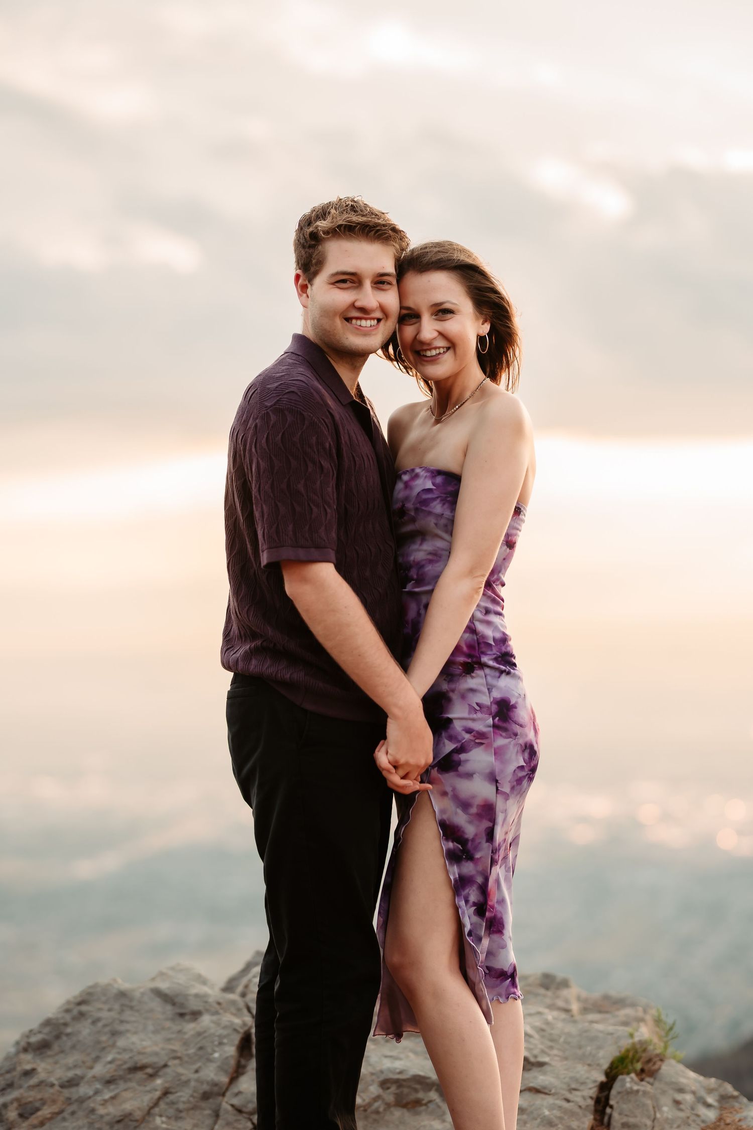 A couple embraces joyfully on a mountain overlook at dusk.