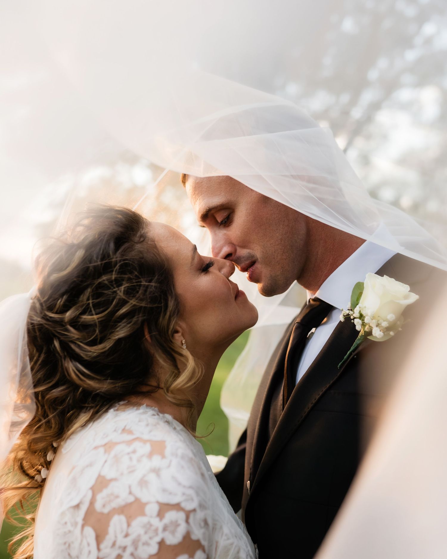 Bride and groom sharing a romantic kiss under a flowing veil on their wedding day.