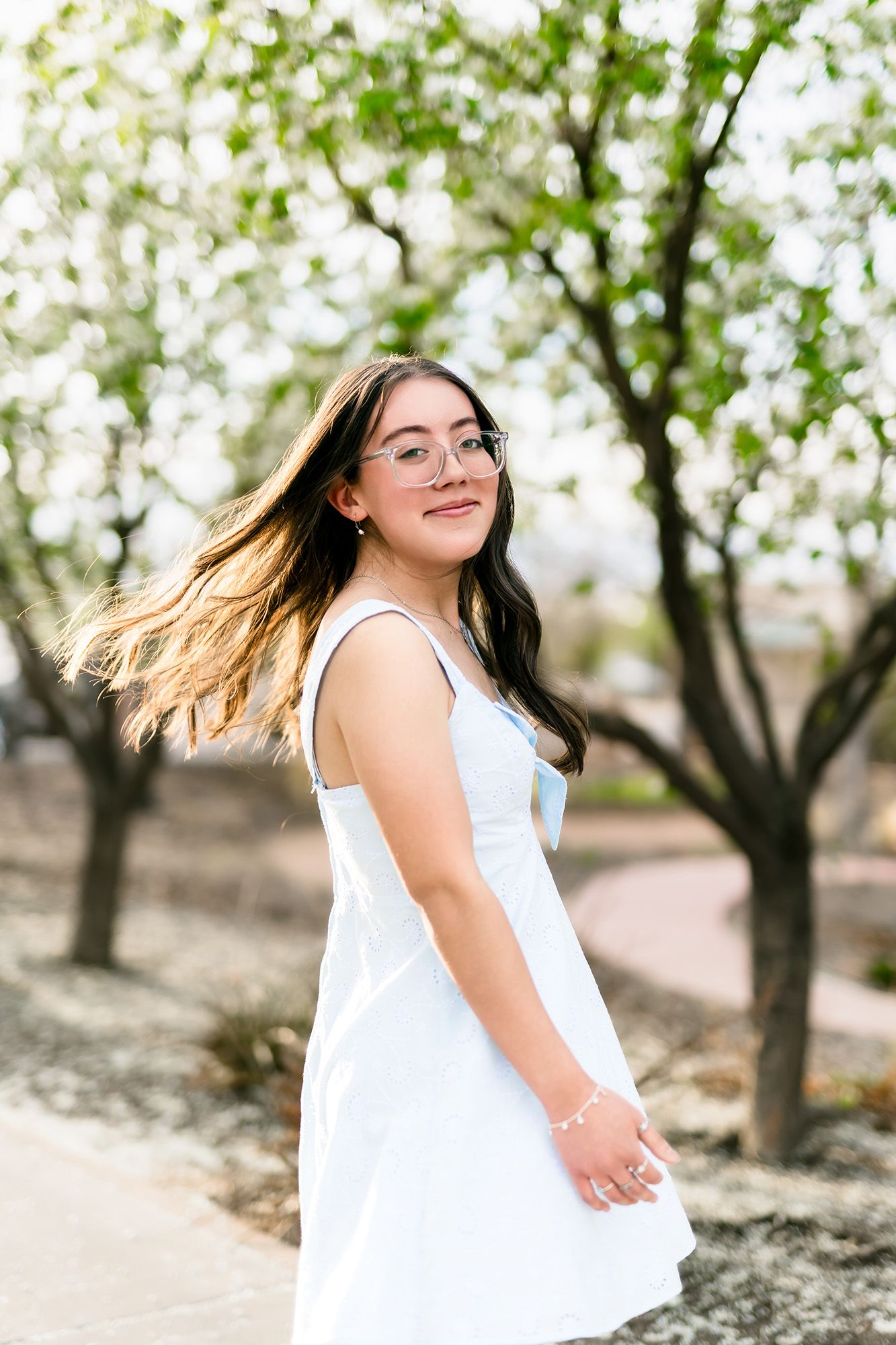 A series of outdoor portraits showing someone in a white dress twirling and smiling among blooming trees in soft lighting.