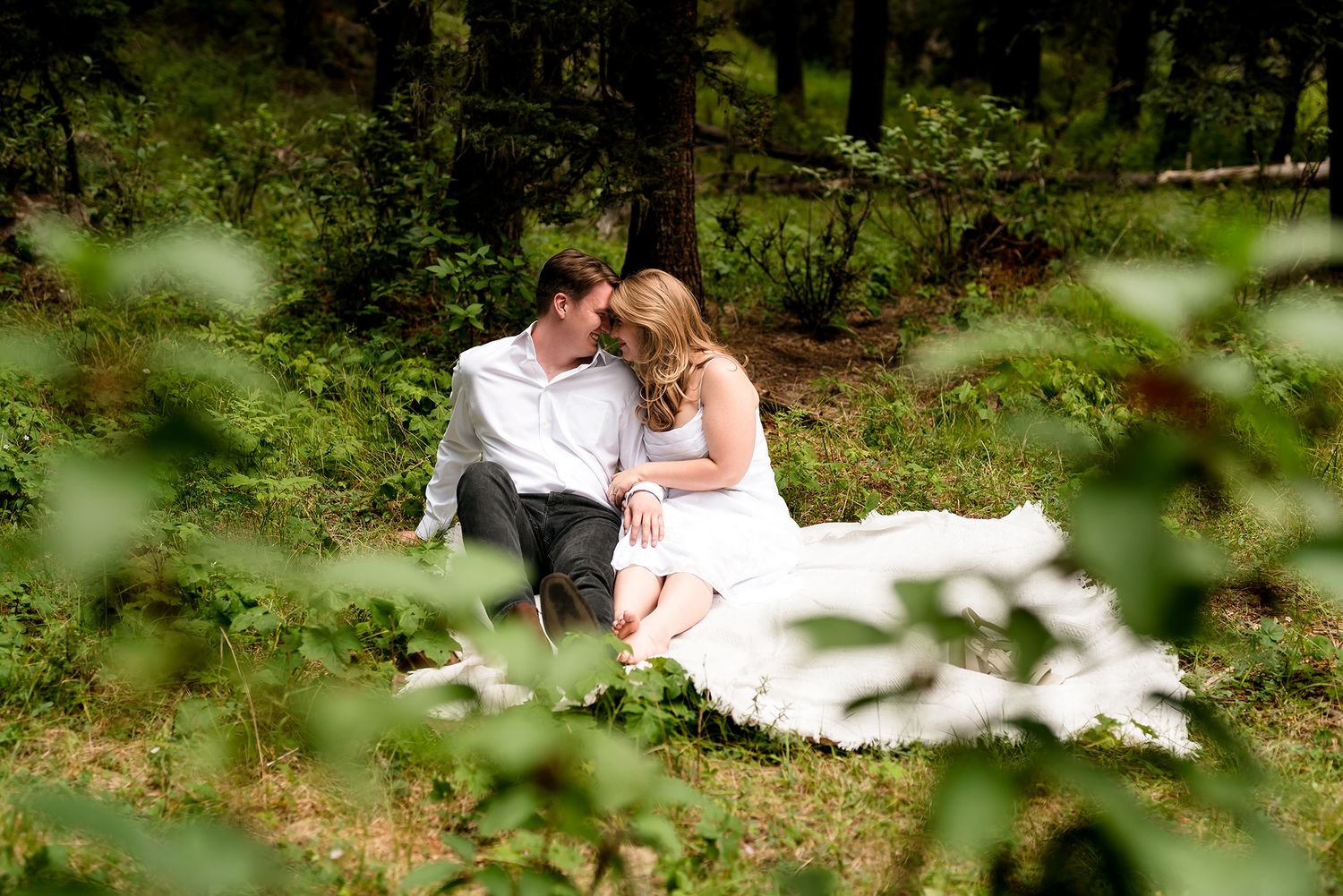 Bride and groom sitting together in a lush forest setting, sharing an intimate moment in wedding attire.
