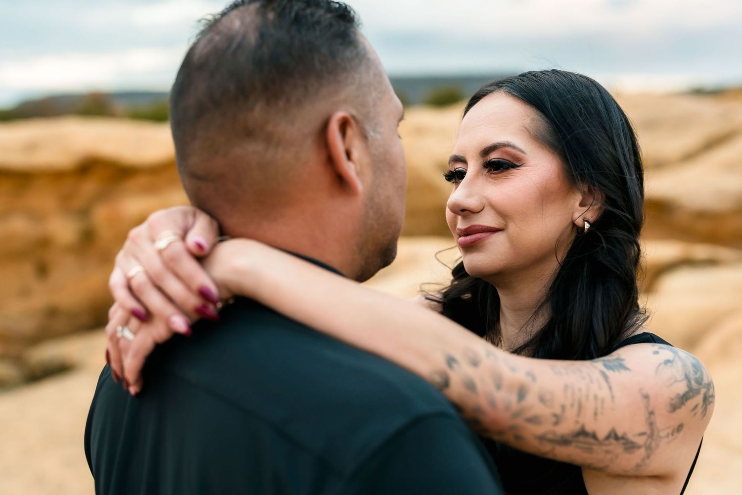 Woman with tattoos smiling at man during outdoor desert engagement photo session.
