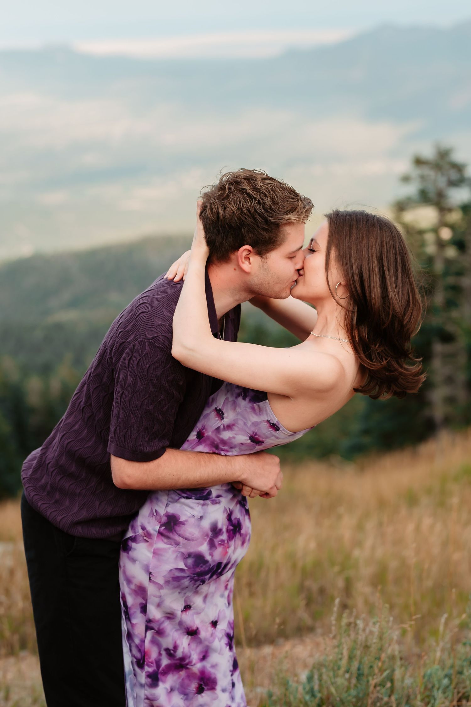 A romantic kiss shared on a mountaintop with scenic valley views.