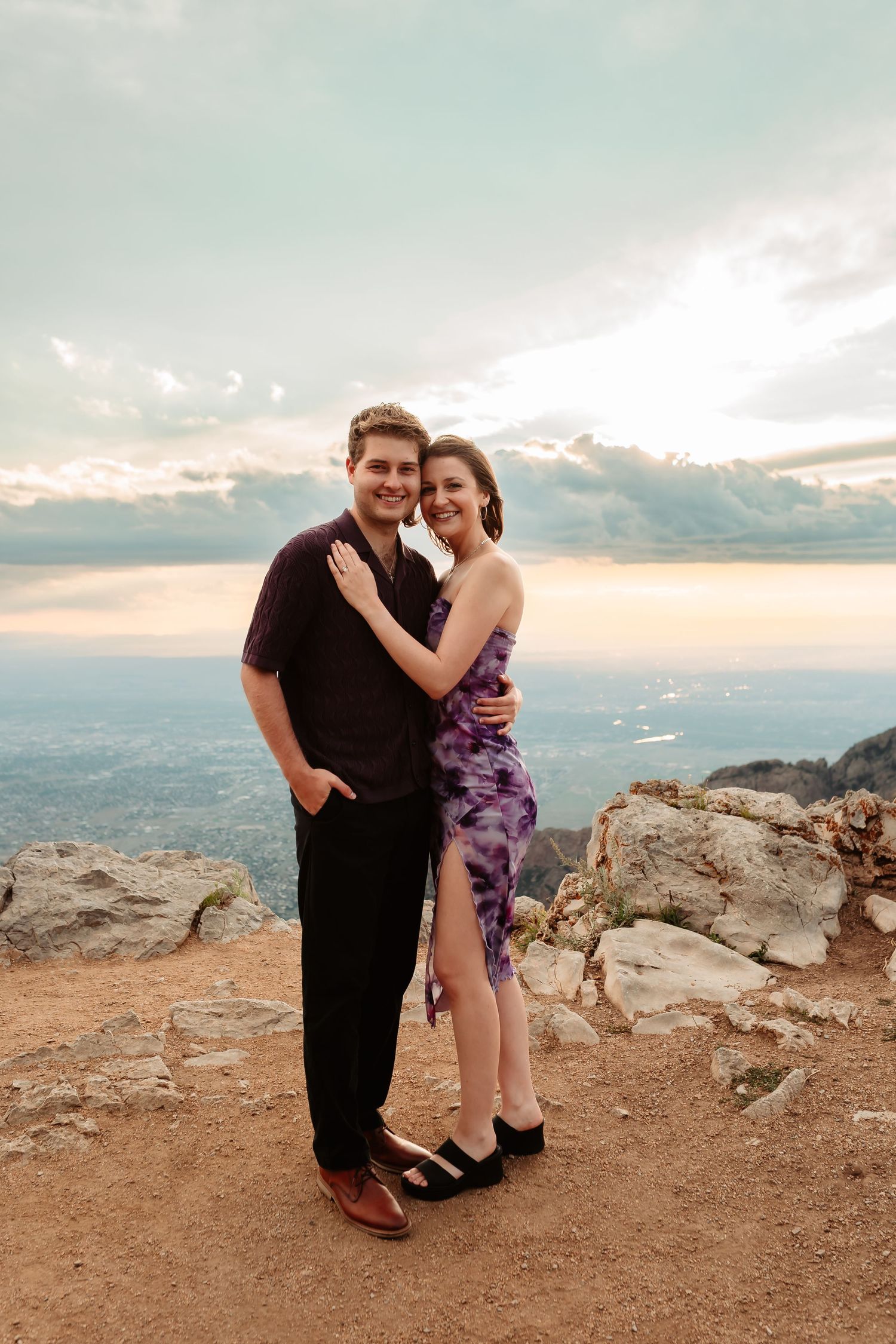 Romantic couple embrace on a mountain overlook during golden hour.