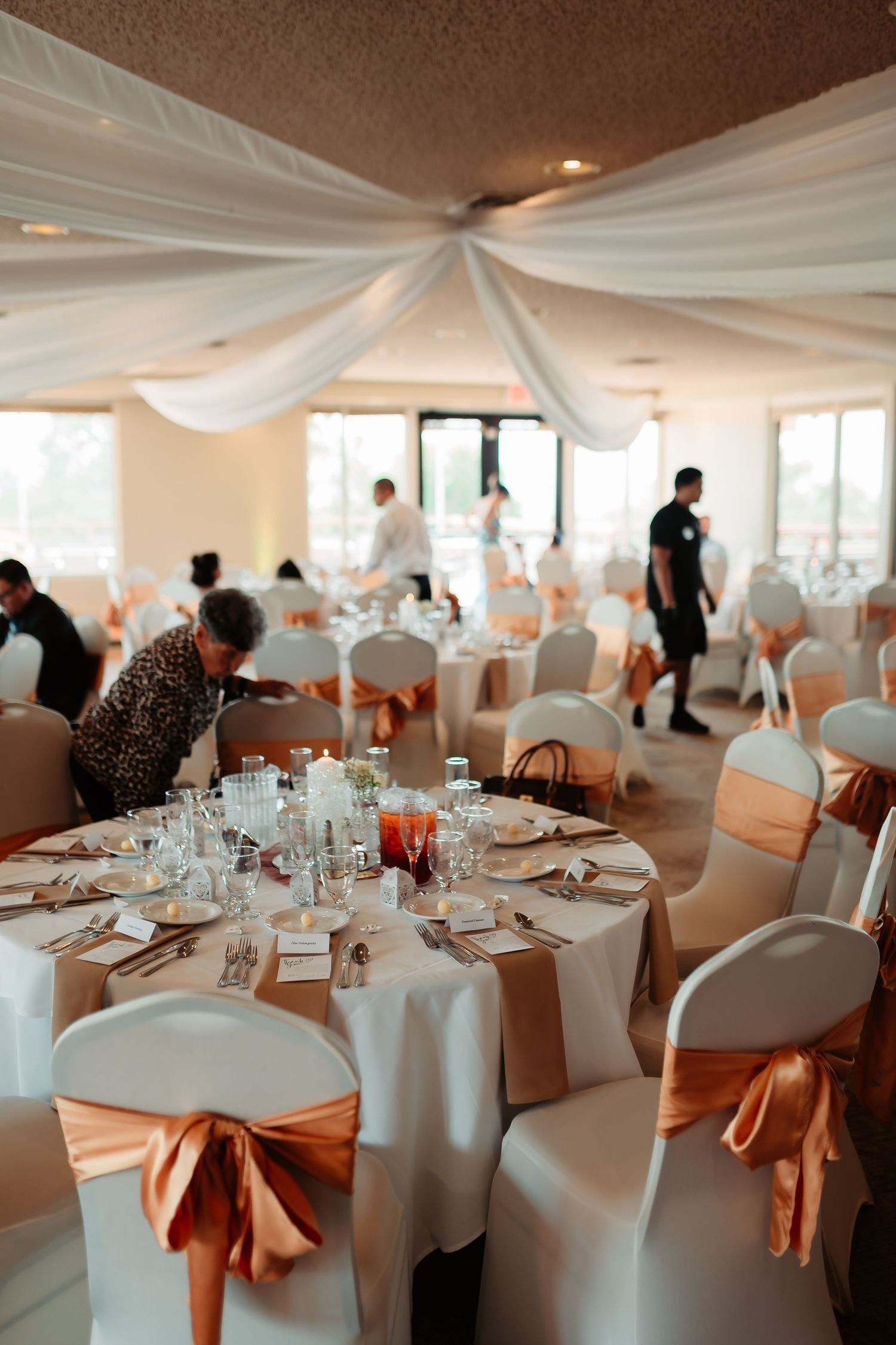 Elegant wedding reception venue with white draped ceiling, round tables, white chair covers and rose gold satin bows.