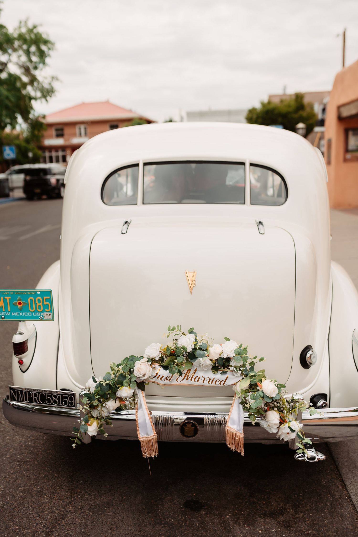 Back view of a vintage white car decorated with floral arrangements for a wedding.