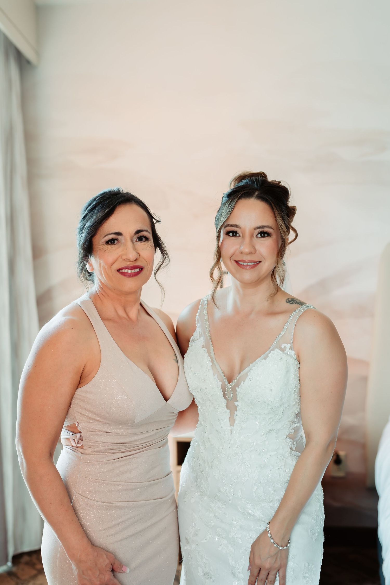 Two people in formal attire share sweet smiles and laughter together in front of a light colored wall.