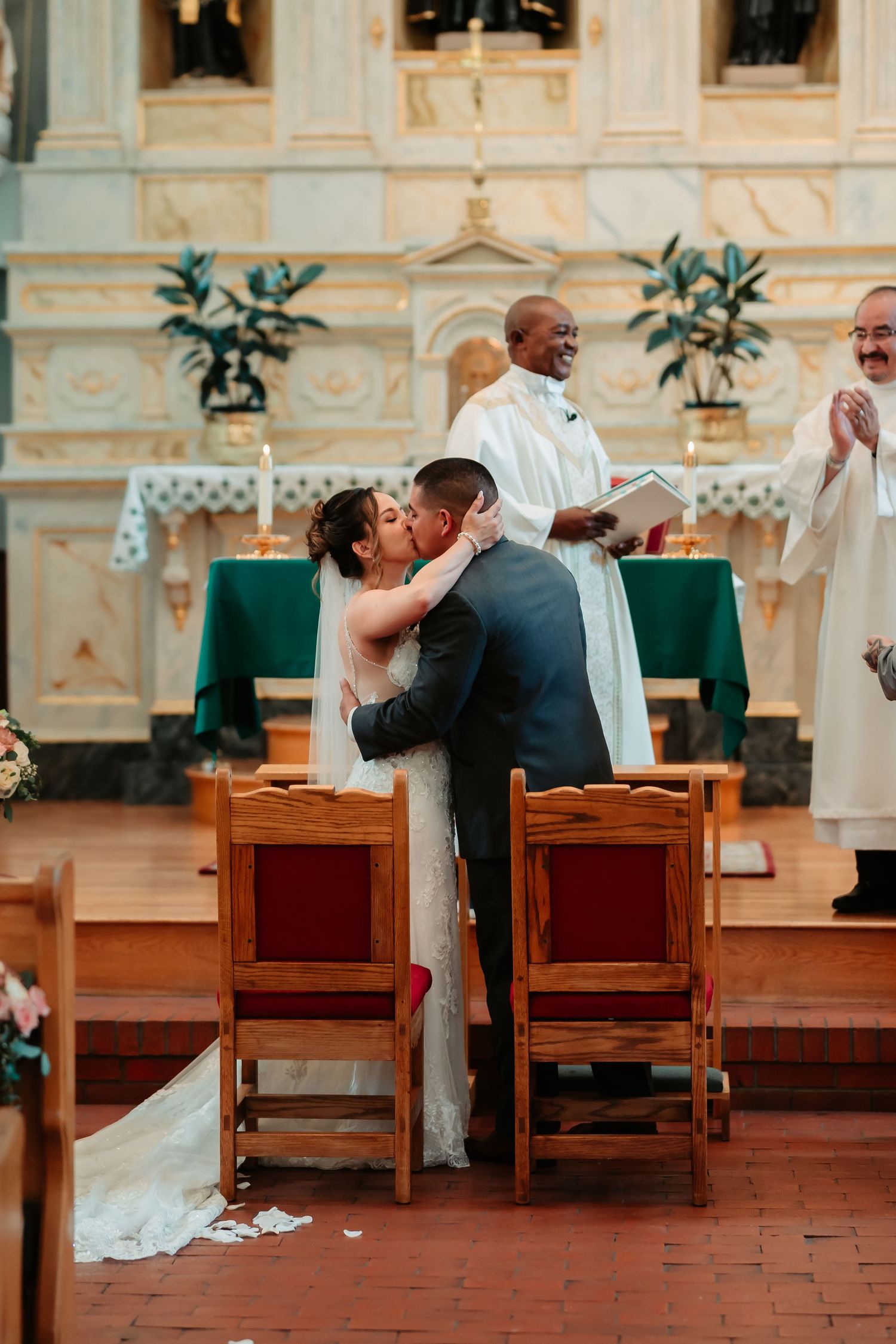 Wedding party seated in wooden chairs at the front of a church with terracotta floors.