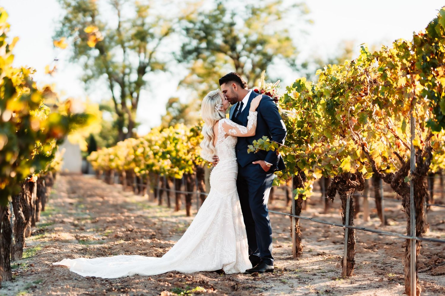 A couple shares a romantic moment among golden autumn vineyard rows during a sunset wedding photo session.