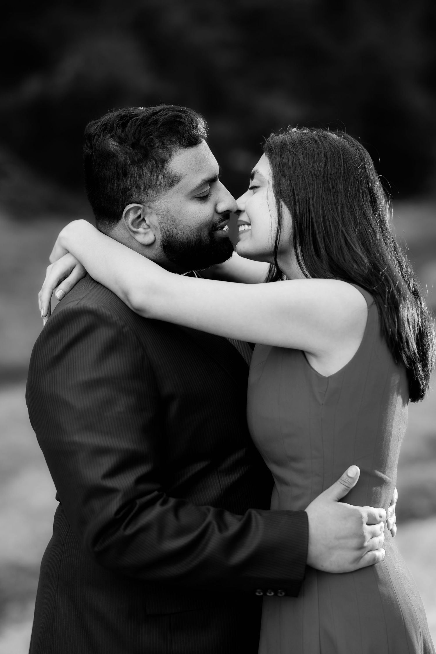 A black and white photo of a couple sharing an intimate embrace outdoors.