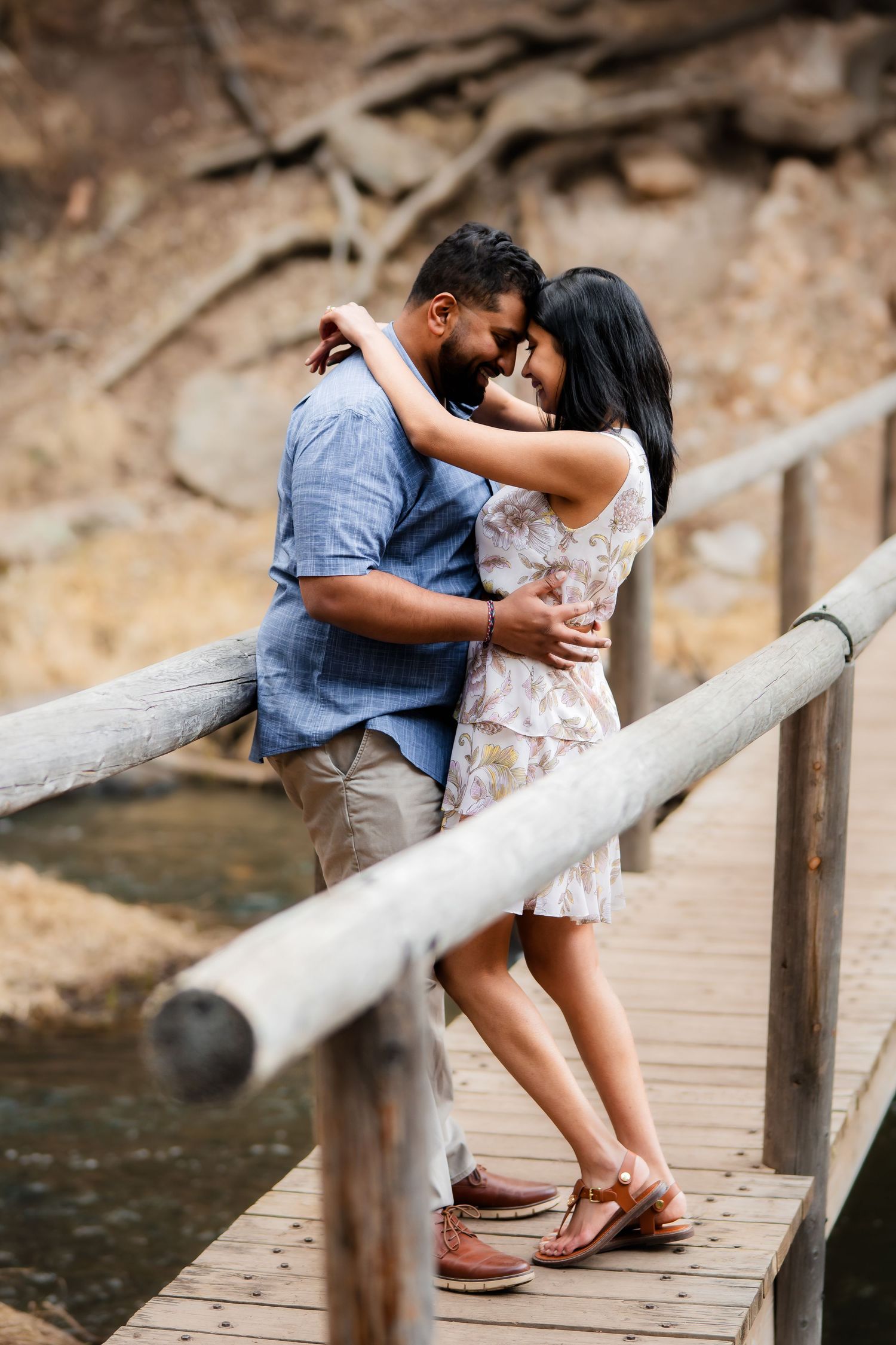 A romantic couple embraces on a wooden dock by the water in casual summer attire.
