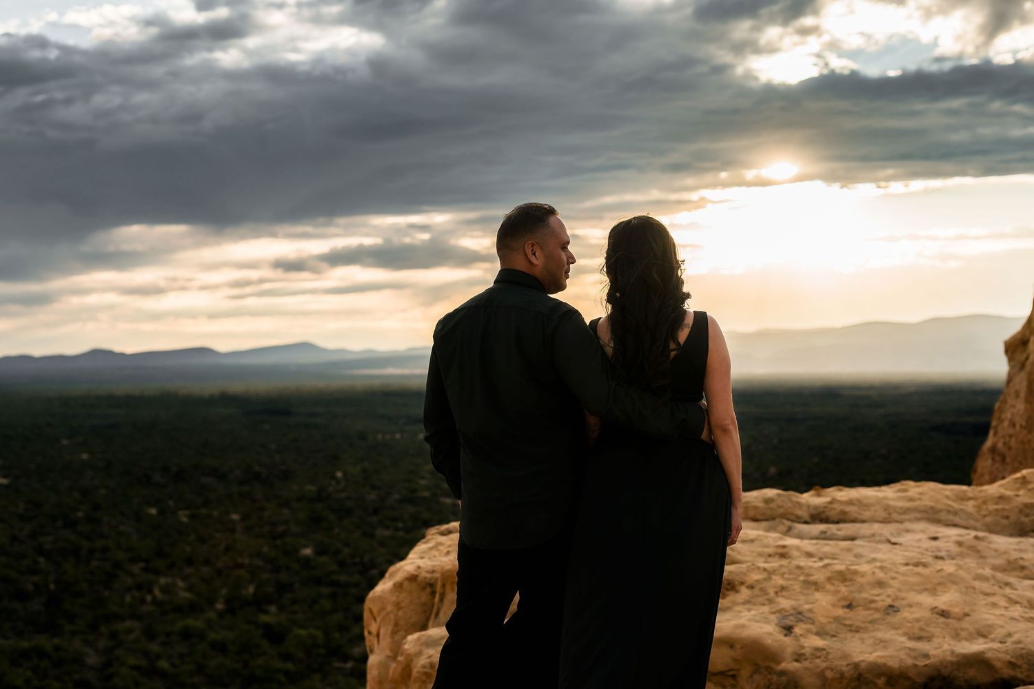 Couple in black silhouetted against a breathtaking desert sunset with mountains visible in the distance.