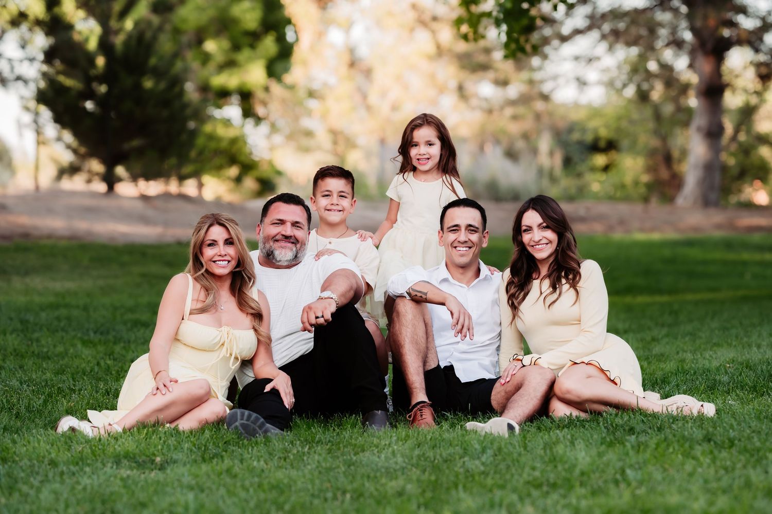 A series of five outdoor family photos taken in a grassy park setting with natural lighting and casual poses.