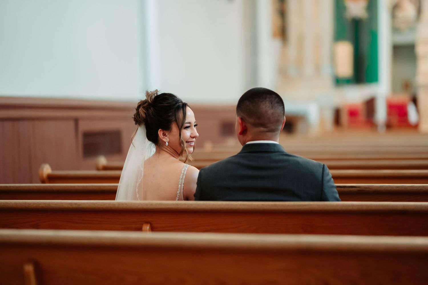 Happy couple sitting together in wooden church pews on their wedding day.