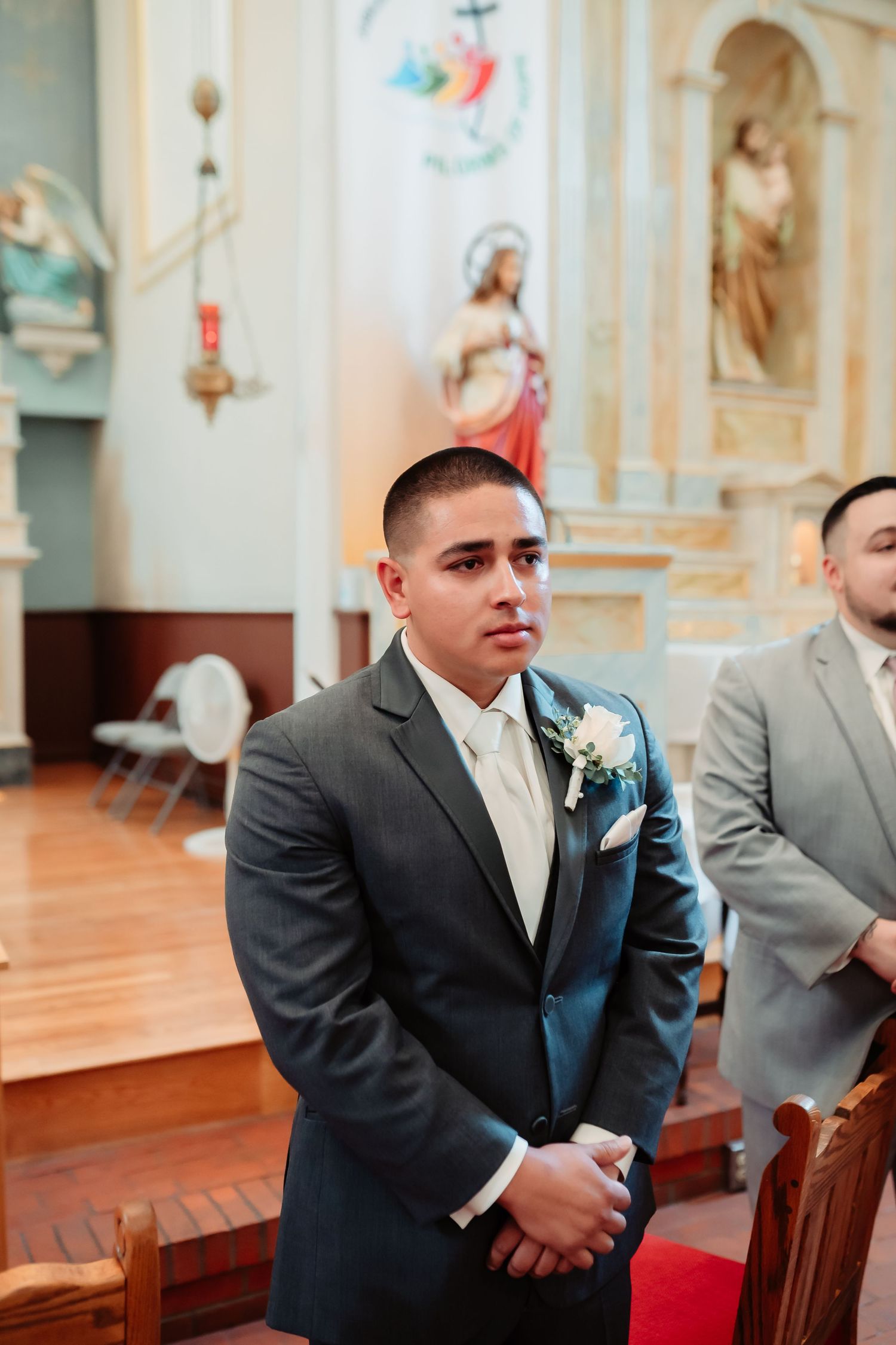 Grey-suited groomsmen seated in traditional church pews during ceremony.