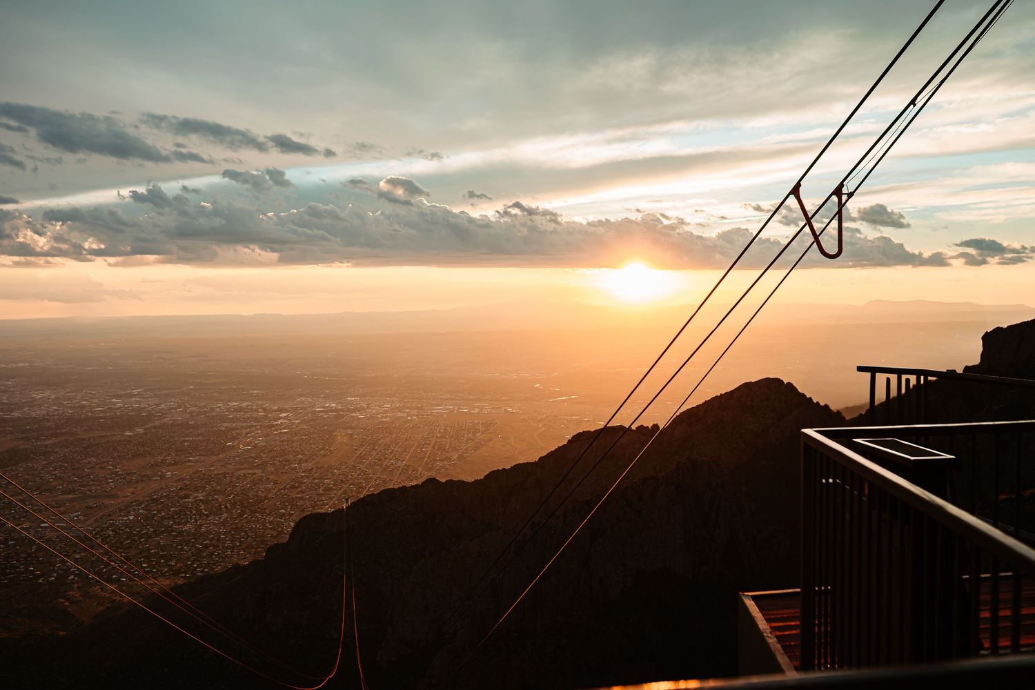 Mountain landscape at sunset with power lines silhouetted against vibrant orange and purple sky.