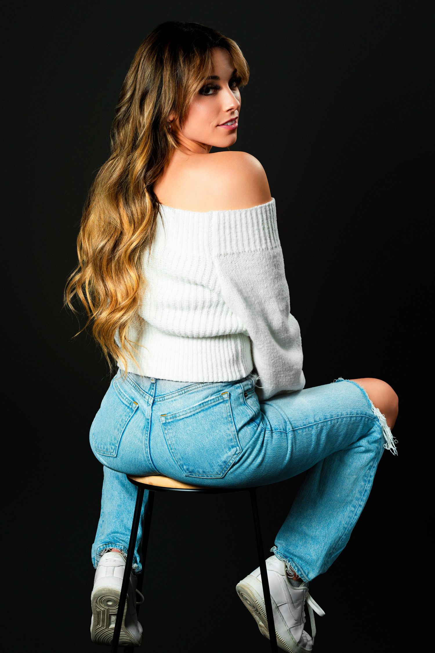 Fashion portrait showing a white turtleneck sweater paired with light blue denim jeans against a dark background.