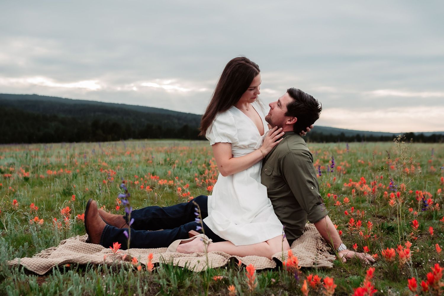 Romantic couple sharing an intimate moment on blanket in blooming red poppy field during sunset.