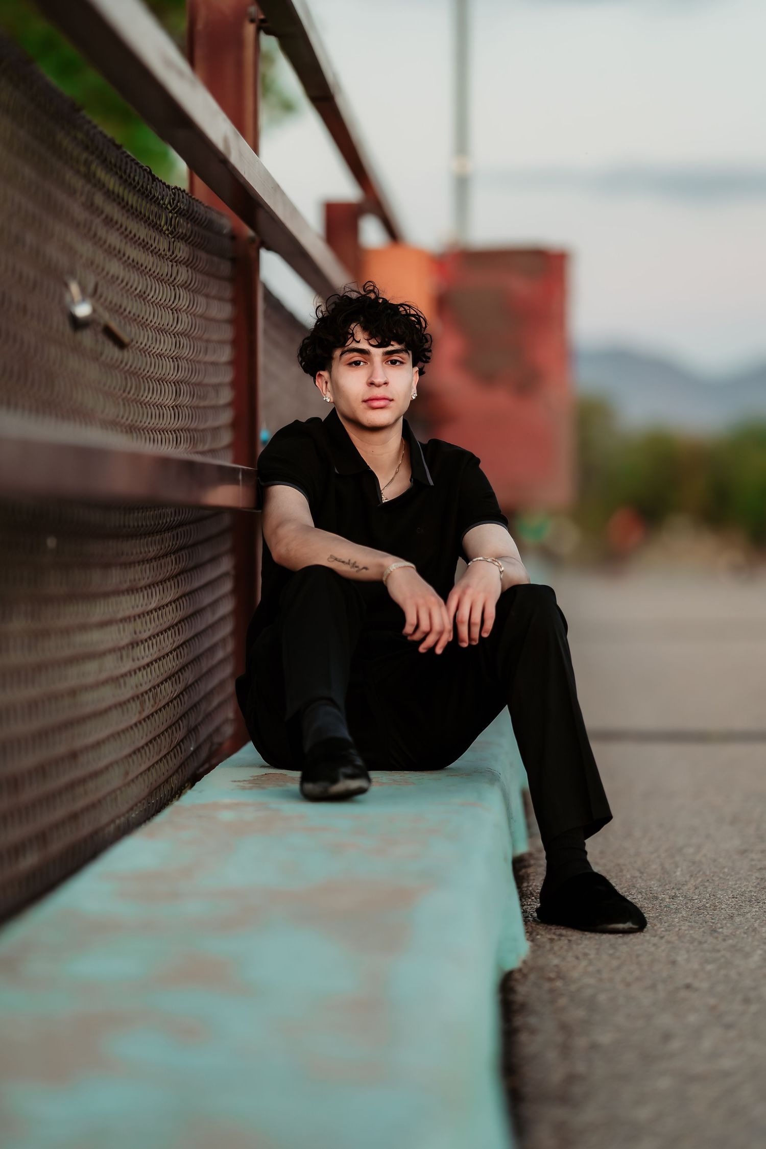 Artistic portrait taken along a bridge wall with turquoise accents at dusk.
